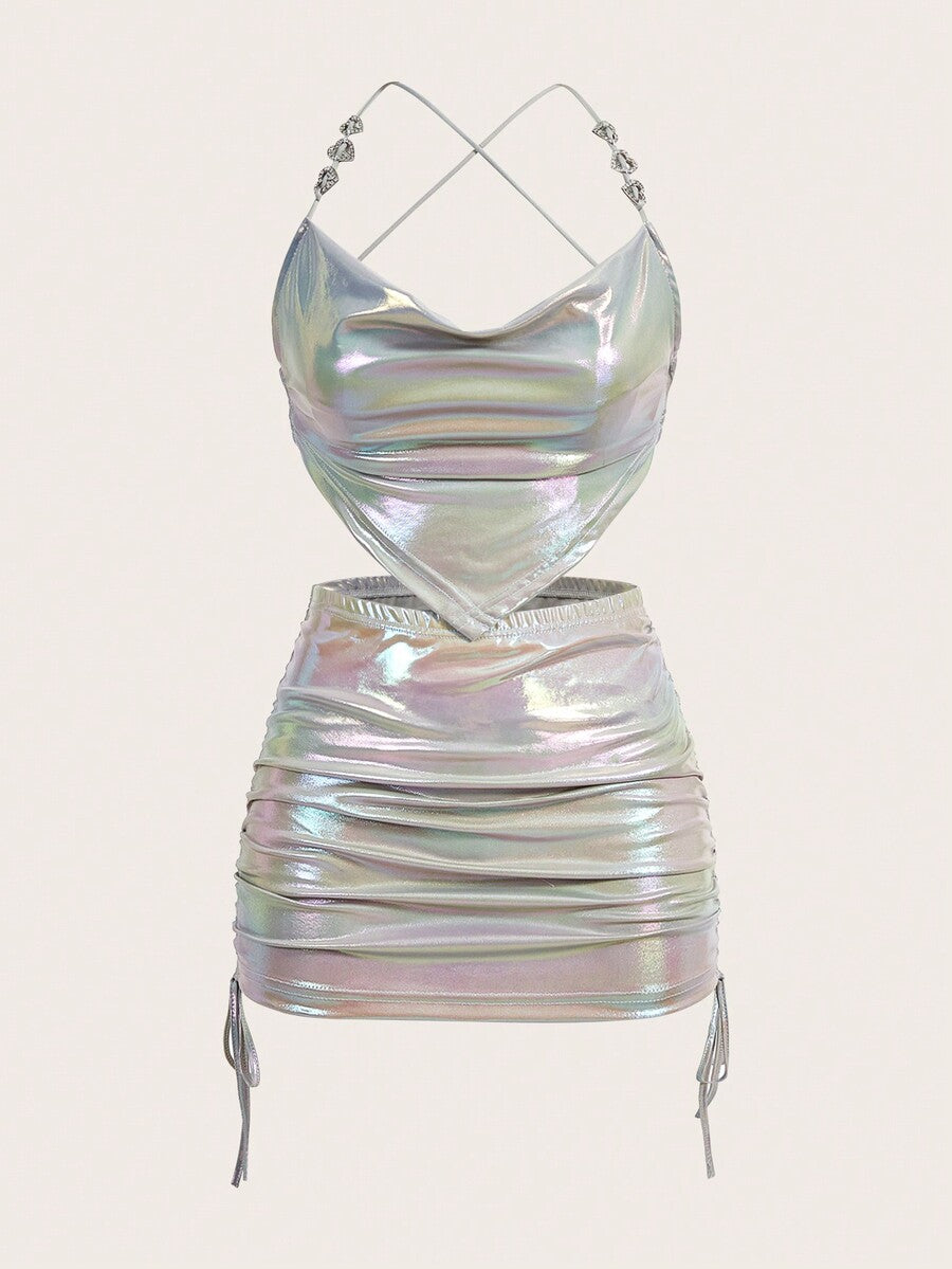Holographic metallic two-piece set with a spaghetti strap hanky hem crop cami top and drawstring side skirt, featuring ruched details and rhinestone accents.