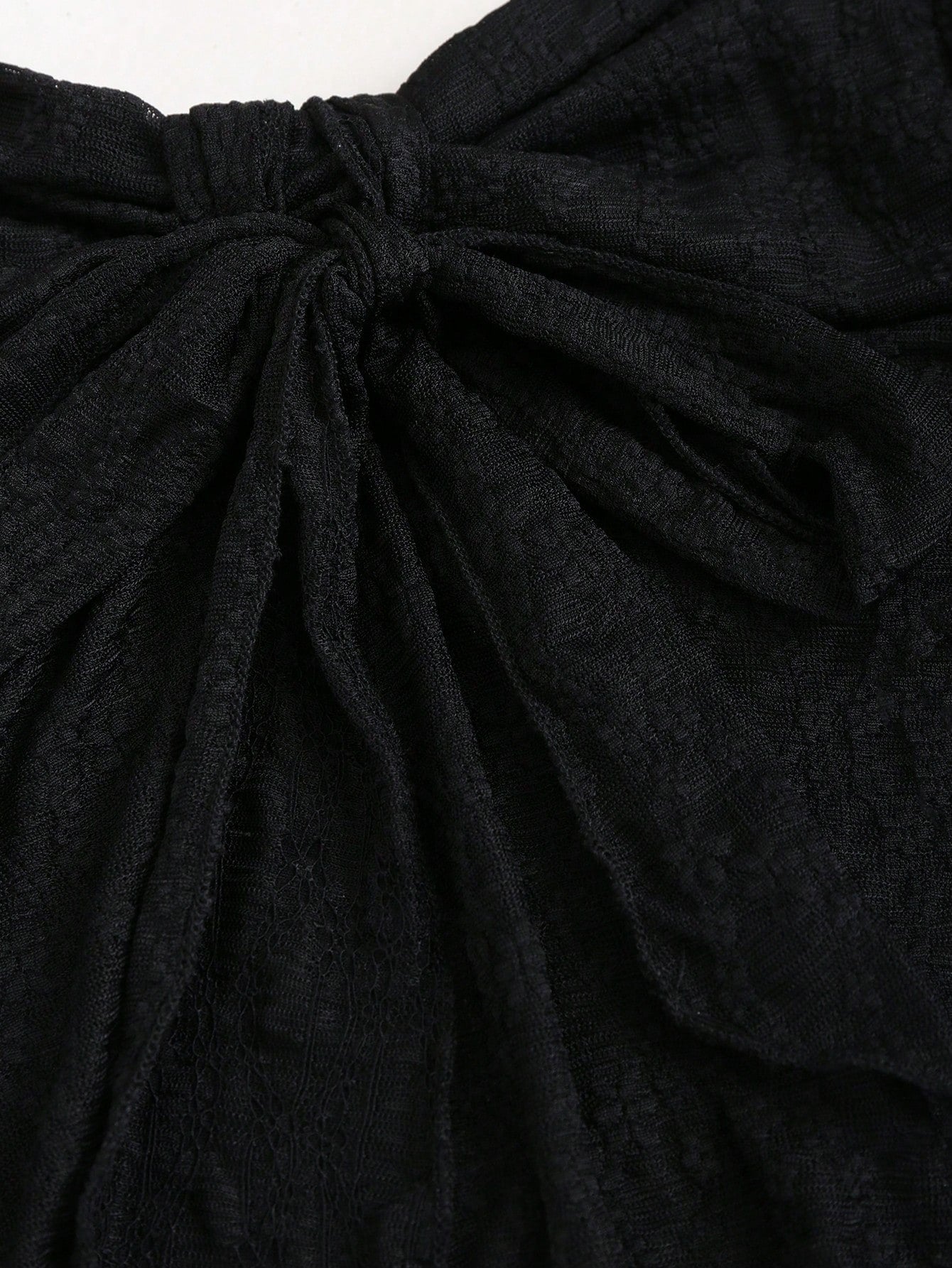 Women's black lace halter crop top with contrast bow front, backless styling, semi-sheer finish, and asymmetrical hem