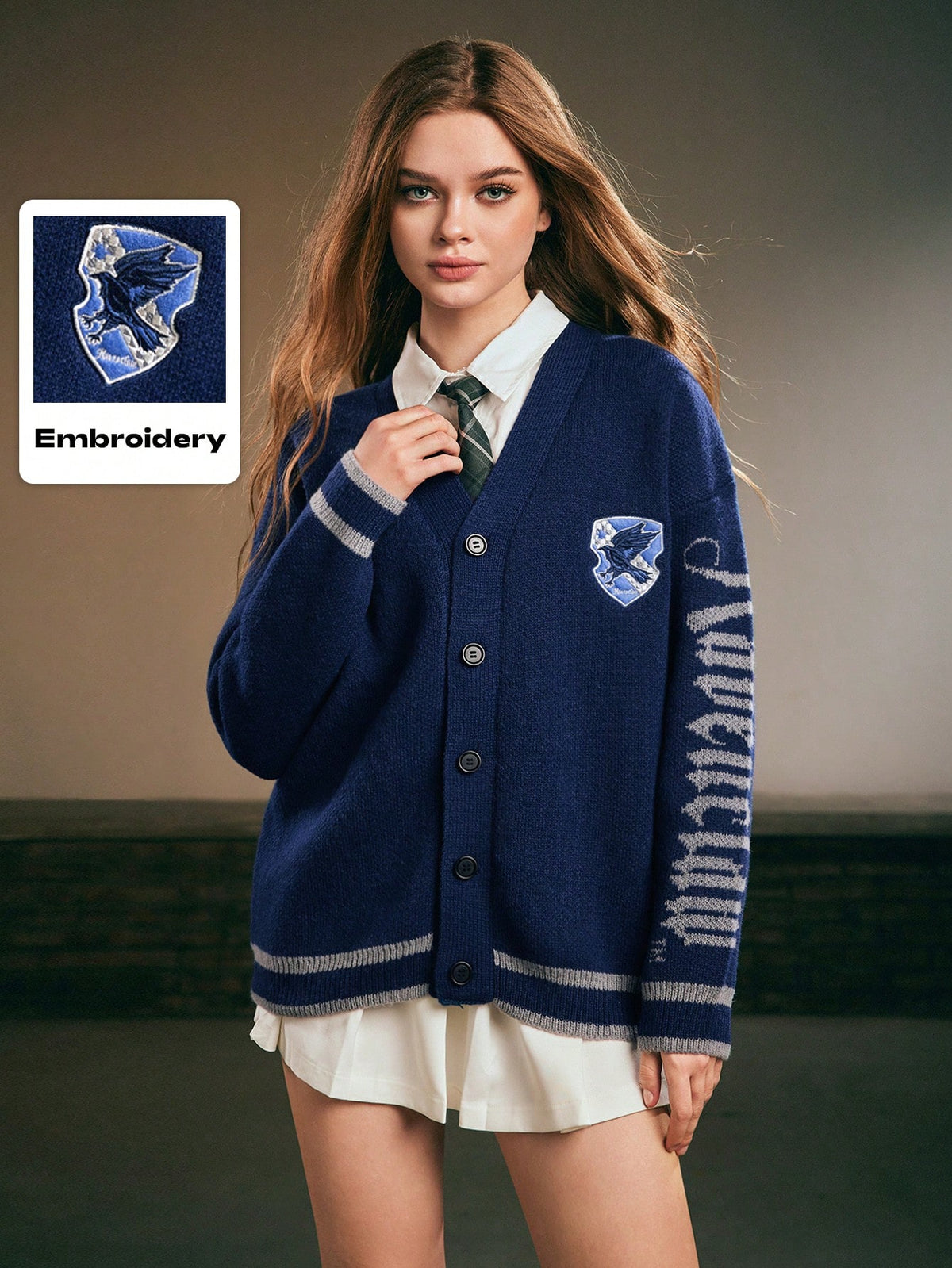 Women's blue loose knit cardigan sweater featuring a V-neckline, button-down front, letter embroidered badge, and dropped shoulders.