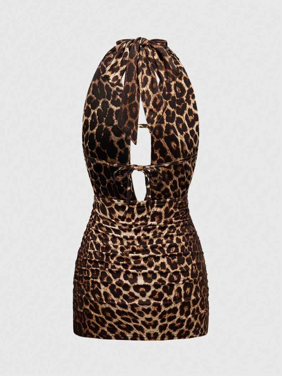 Black backless halter mini dress with ruched details, cut-out back, tied back design, and rhinestone cross pendant accent.