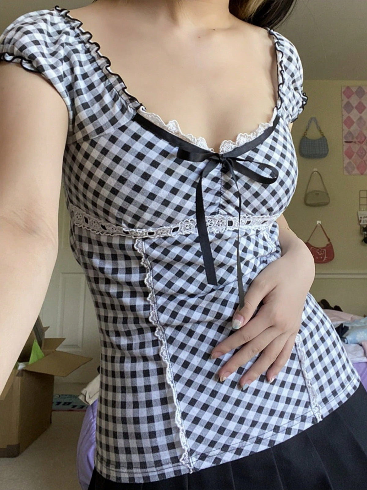 Women's black and white plaid short sleeve blouse featuring a tie-front front bow, contrast lace frill trim, raglan sleeves, and sweetheart neckline.