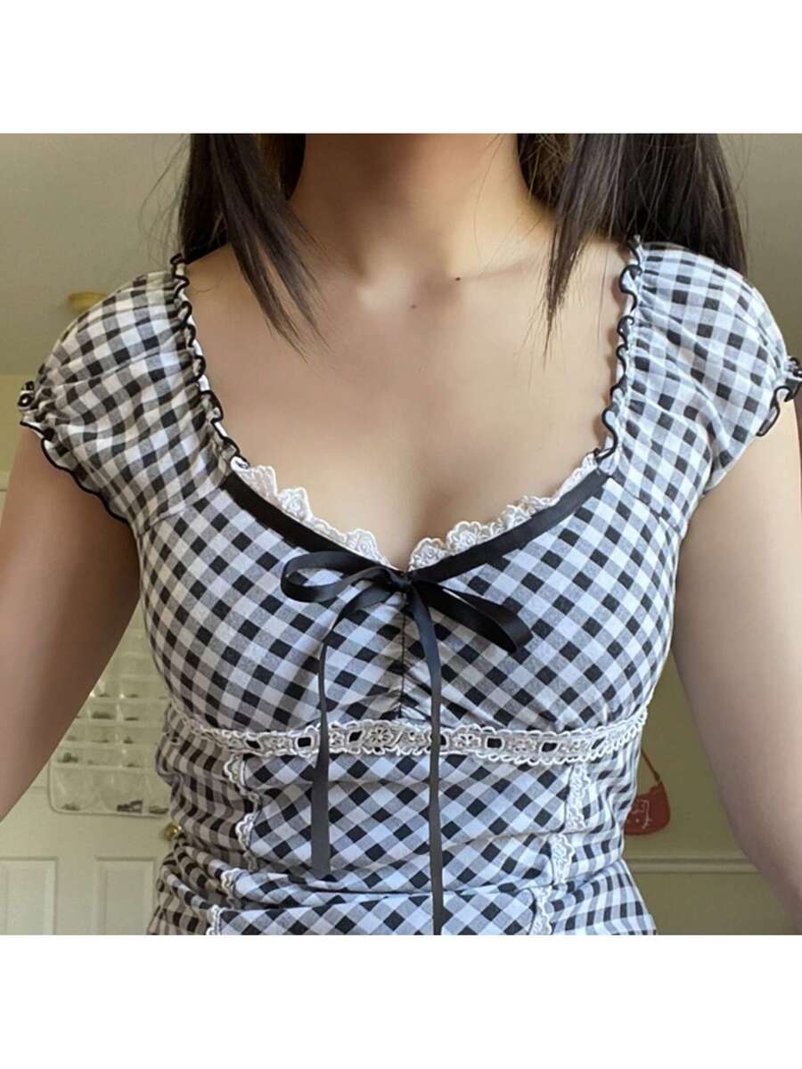 Women's black and white plaid short sleeve blouse featuring a tie-front front bow, contrast lace frill trim, raglan sleeves, and sweetheart neckline.