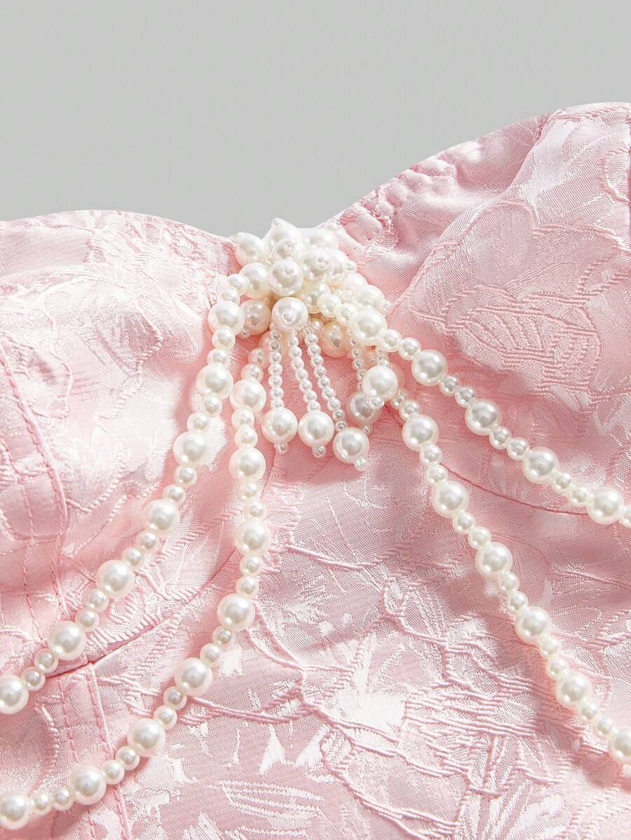 Women's apricot strapless vintage palace style blouse featuring an asymmetrical ruffle hem, backless design, and pearl brooch detail.