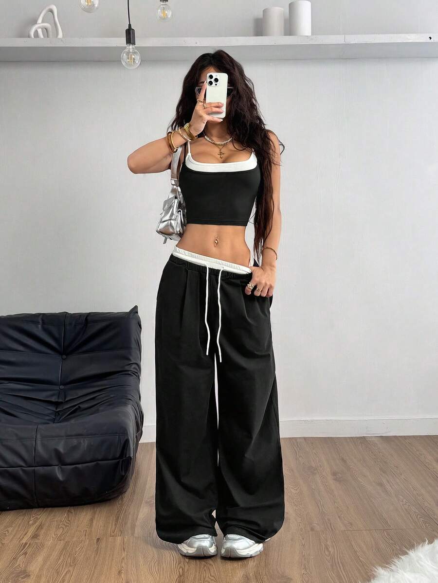 Women's black and white two-piece set featuring a cropped spaghetti strap camisole tank top with contrast binding and matching long drawstring sweatpants with pockets.