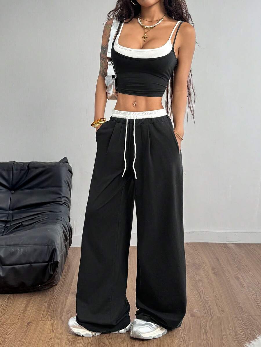 Women's black and white two-piece set featuring a cropped spaghetti strap camisole tank top with contrast binding and matching long drawstring sweatpants with pockets.