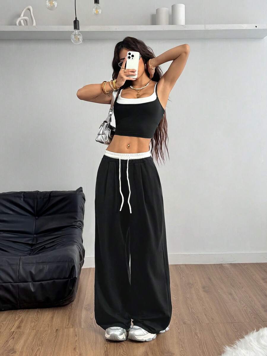 Women's black and white two-piece set featuring a cropped spaghetti strap camisole tank top with contrast binding and matching long drawstring sweatpants with pockets.