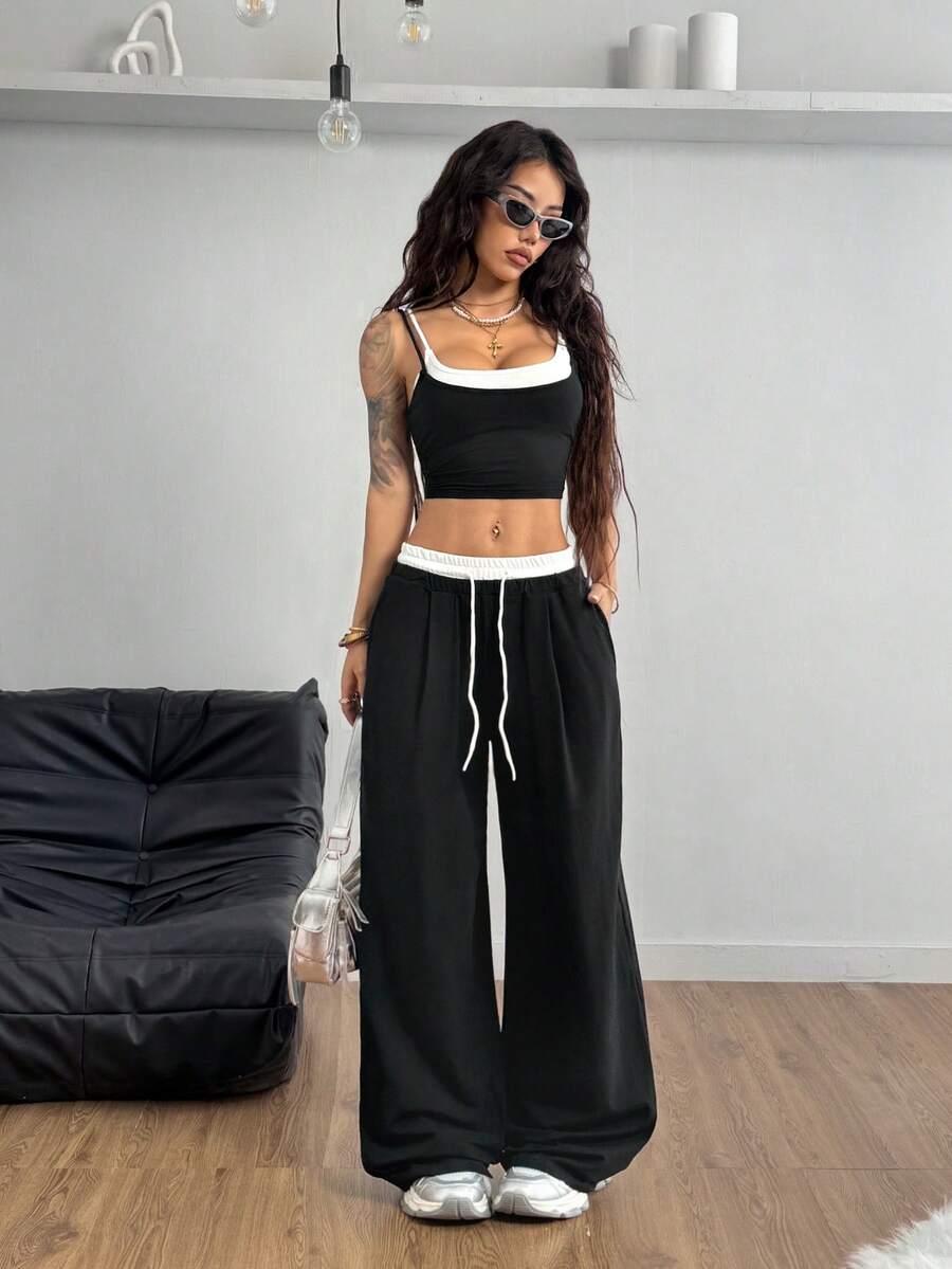 Women's black and white two-piece set featuring a cropped spaghetti strap camisole tank top with contrast binding and matching long drawstring sweatpants with pockets.