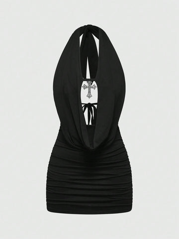 Black backless halter mini dress with ruched details, cut-out back, tied back design, and rhinestone cross pendant accent.