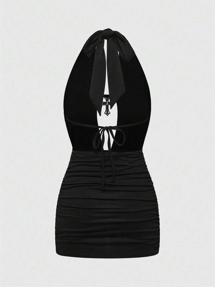 Black backless halter mini dress with ruched details, cut-out back, tied back design, and rhinestone cross pendant accent.