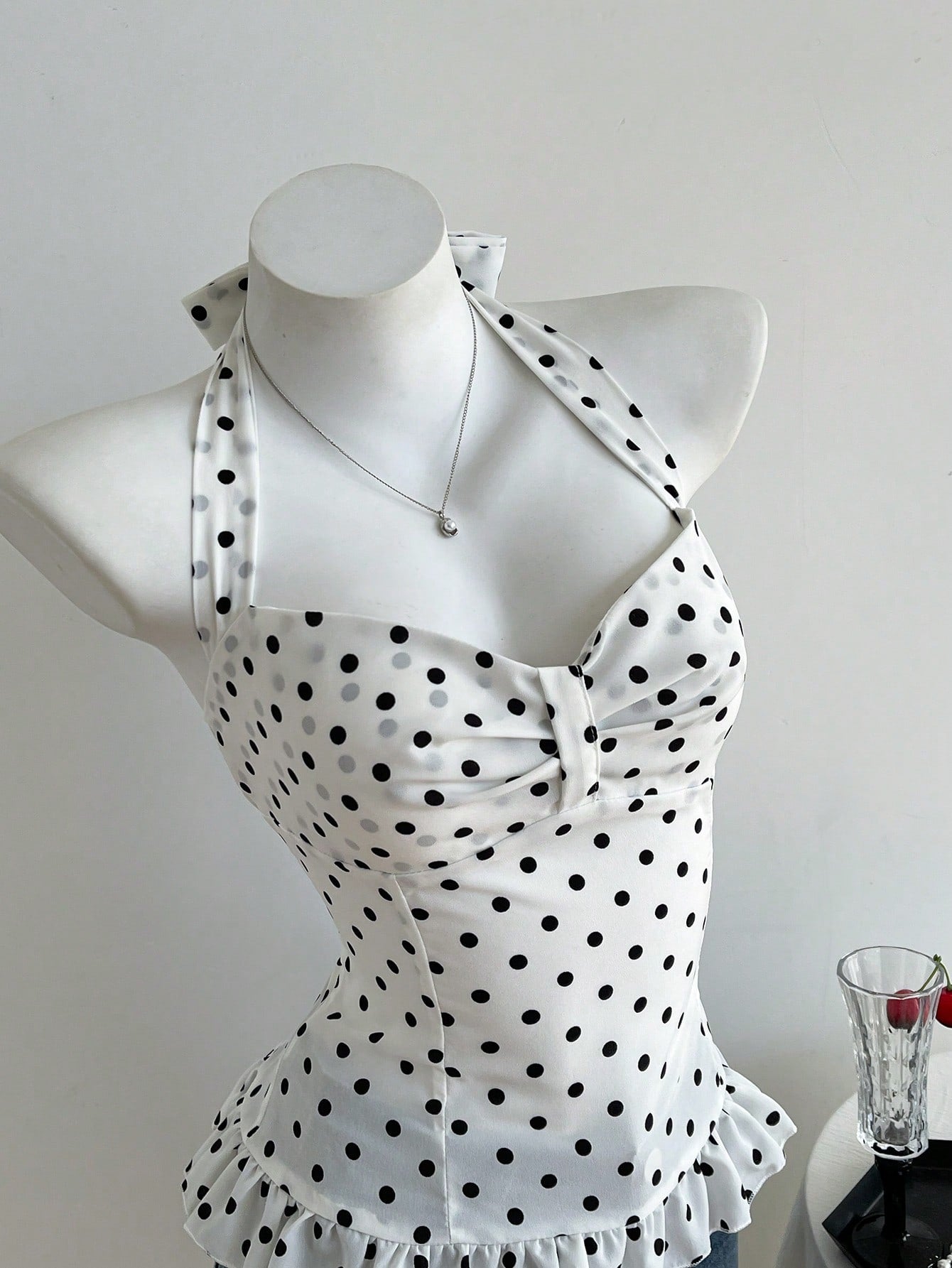 Women's polka dot halter camisole with bow bust detail, ruched and shirred design, slim crop fit, and flared ruffle hem.