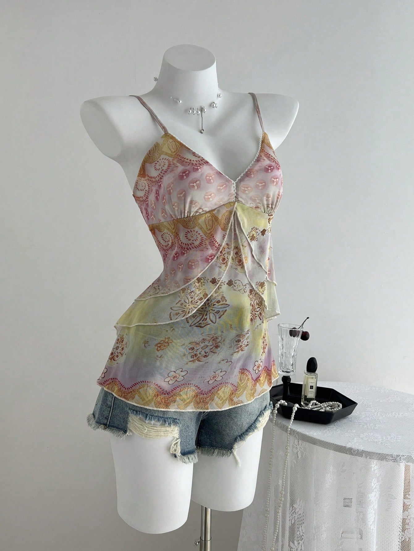 Women's boho spaghetti strap cami with multicolor all-over plant print, contrast lace detail, ruffle tiered hem, and slim fit silhouette.