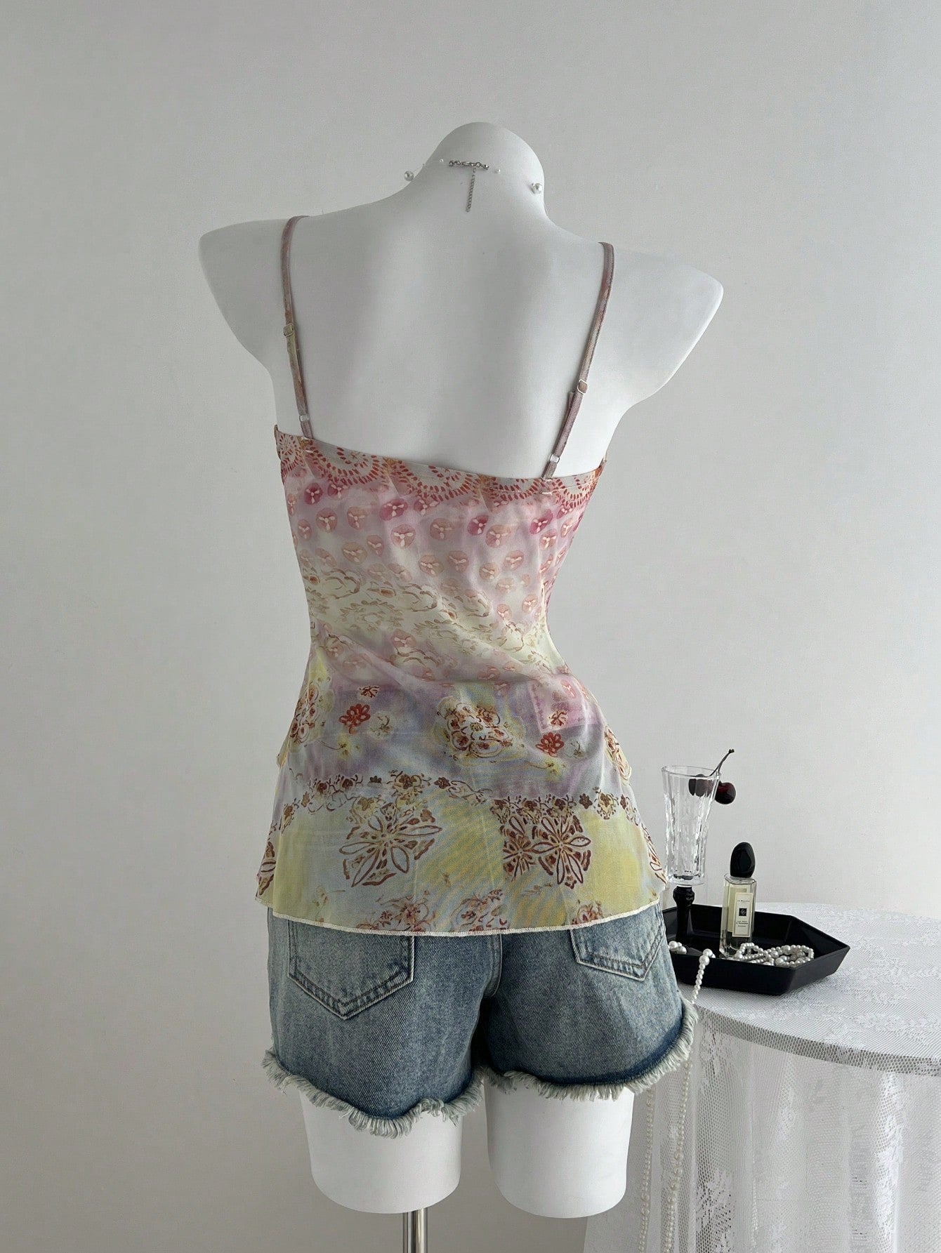 Women's boho spaghetti strap cami with multicolor all-over plant print, contrast lace detail, ruffle tiered hem, and slim fit silhouette.
