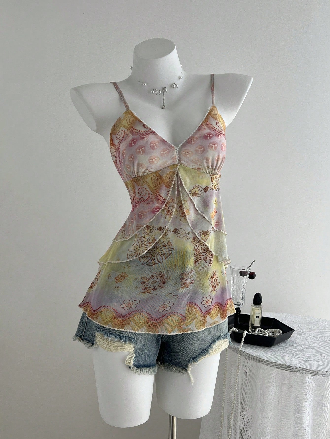 Women's boho spaghetti strap cami with multicolor all-over plant print, contrast lace detail, ruffle tiered hem, and slim fit silhouette.