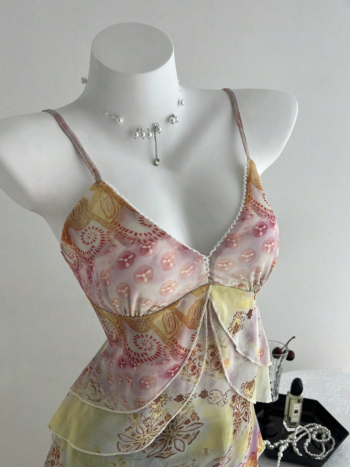 Women's boho spaghetti strap cami with multicolor all-over plant print, contrast lace detail, ruffle tiered hem, and slim fit silhouette.