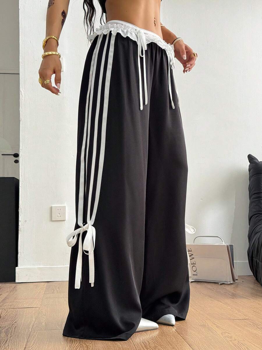 Women's black wide leg casual pants featuring a mid-rise drawstring waistband, contrast lace trim with bow detailing, and side stripes.
