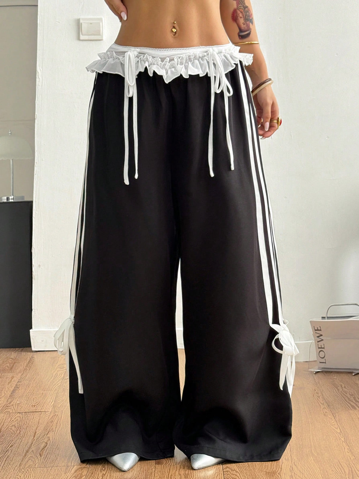 Women's black wide leg casual pants featuring a mid-rise drawstring waistband, contrast lace trim with bow detailing, and side stripes.