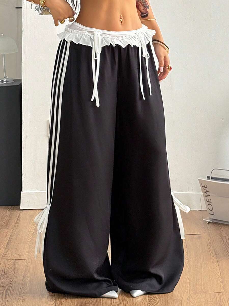 Women's black wide leg casual pants featuring a mid-rise drawstring waistband, contrast lace trim with bow detailing, and side stripes.