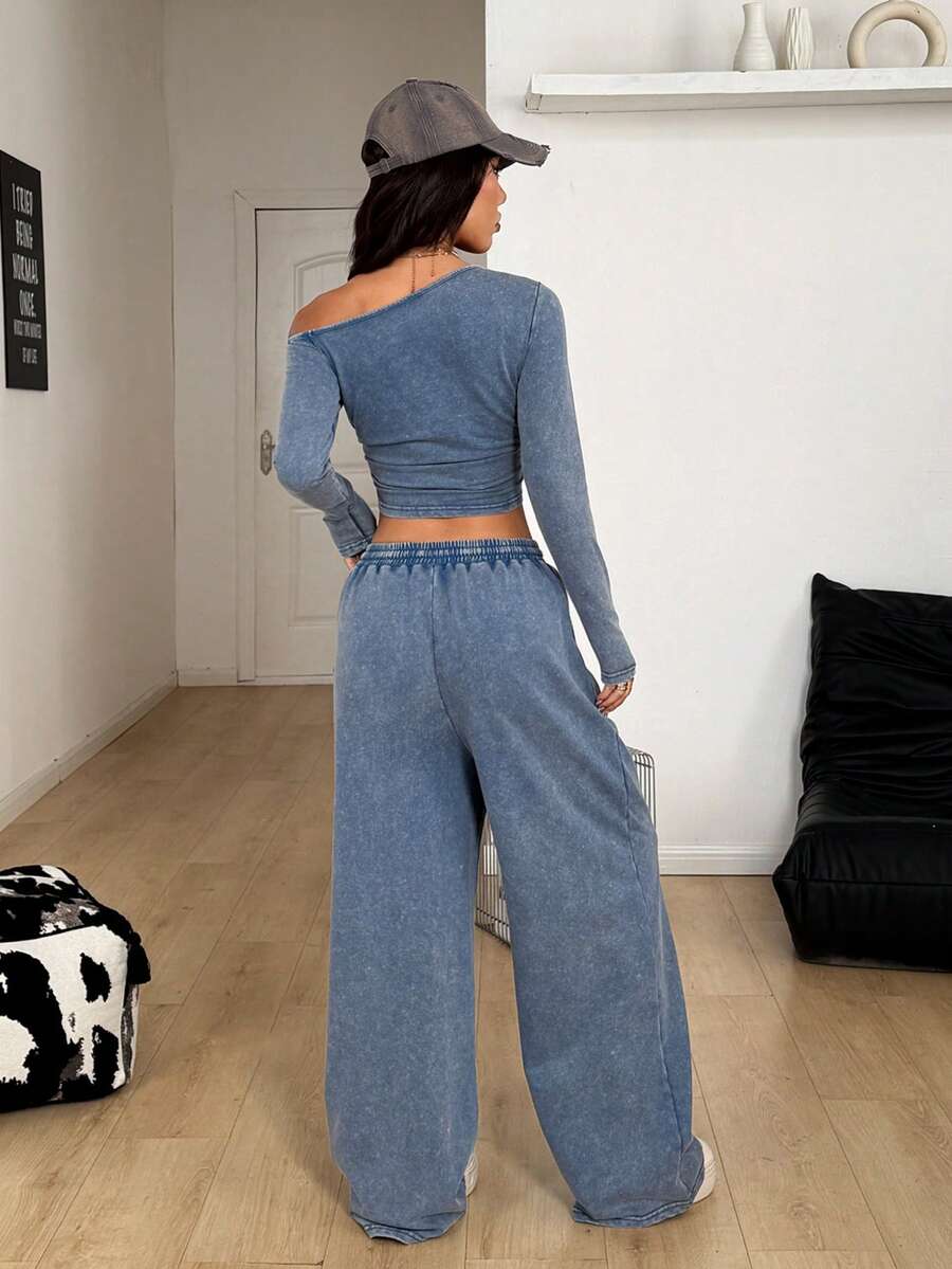 Women's two-piece knit lounge set featuring a black long sleeve asymmetrical crop top and matching high-waisted wide leg sweatpants.