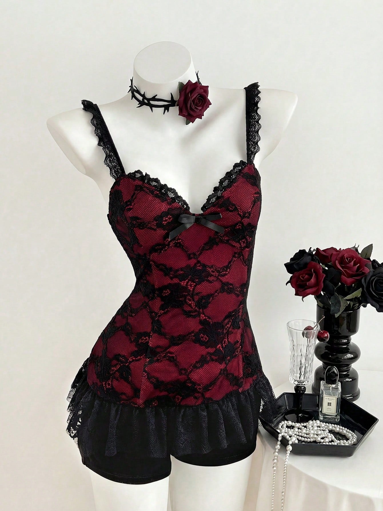 Women's black gothic camisole with contrast lace trim, bow detail, strap neckline, ruffle hem, and slim micro crop fit.