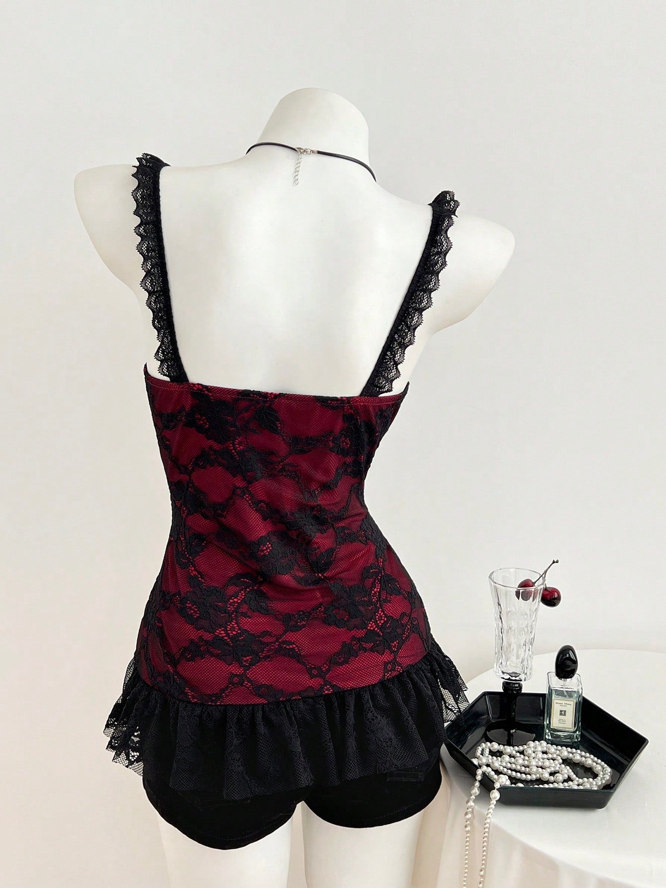 Women's black gothic camisole with contrast lace trim, bow detail, strap neckline, ruffle hem, and slim micro crop fit.