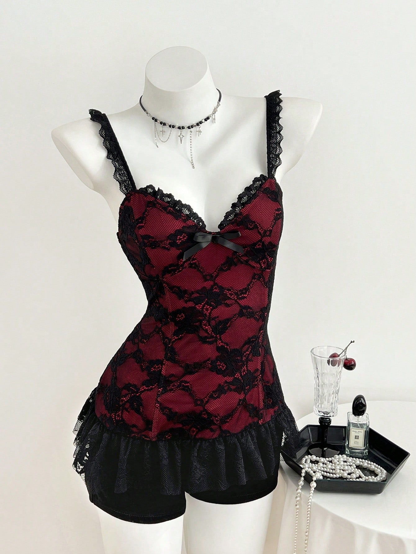 Women's black gothic camisole with contrast lace trim, bow detail, strap neckline, ruffle hem, and slim micro crop fit.