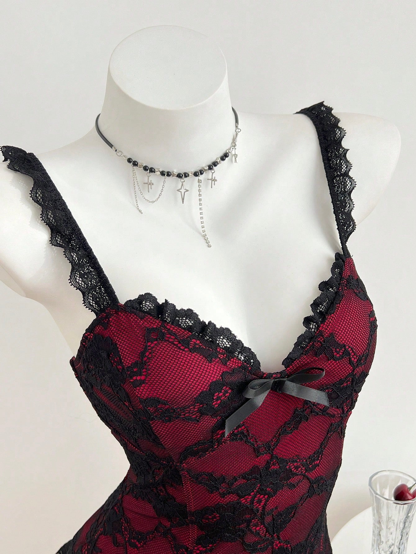 Women's black gothic camisole with contrast lace trim, bow detail, strap neckline, ruffle hem, and slim micro crop fit.