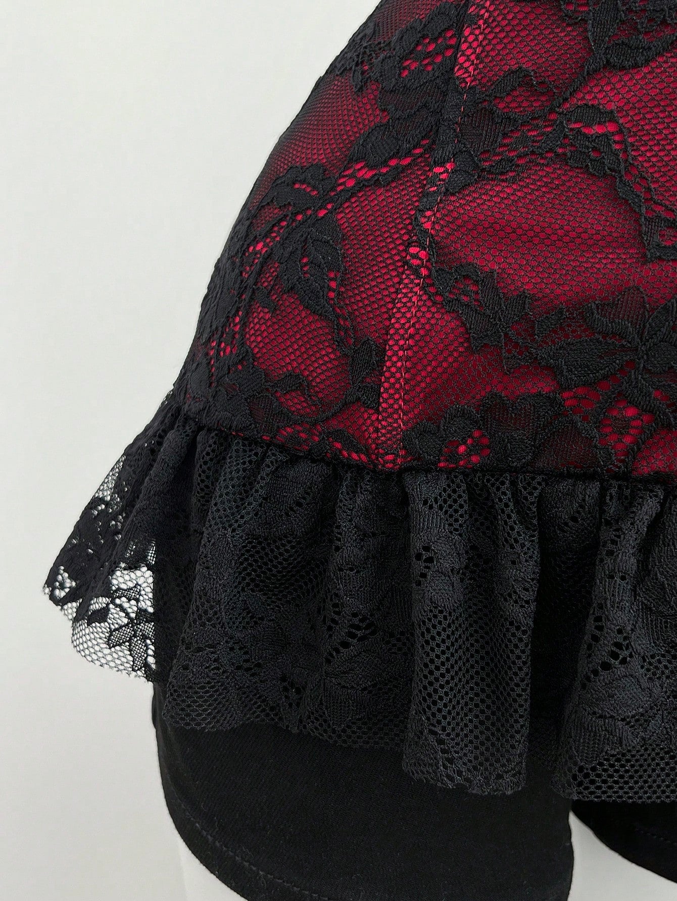 Women's black gothic camisole with contrast lace trim, bow detail, strap neckline, ruffle hem, and slim micro crop fit.