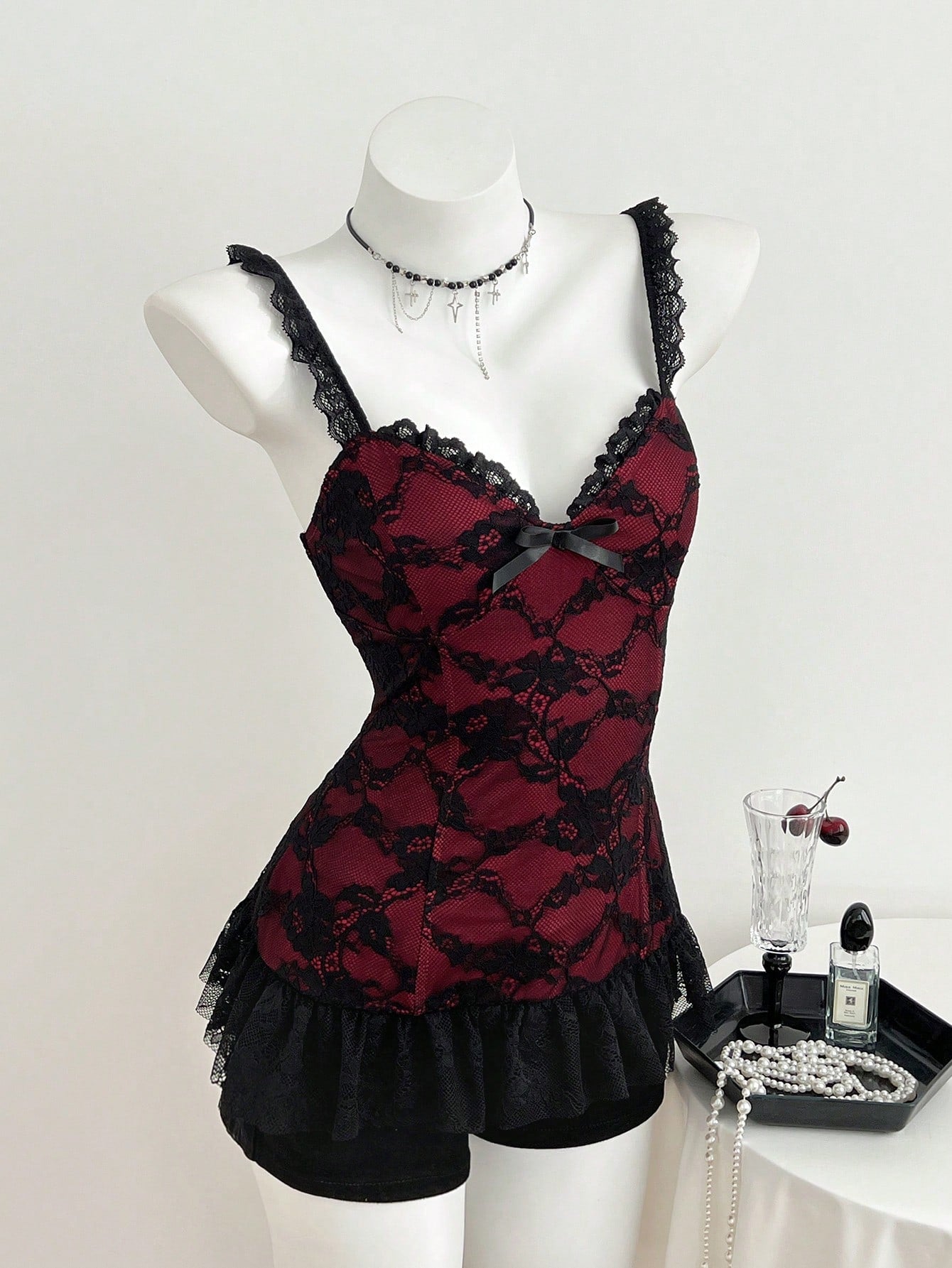 Women's black gothic camisole with contrast lace trim, bow detail, strap neckline, ruffle hem, and slim micro crop fit.
