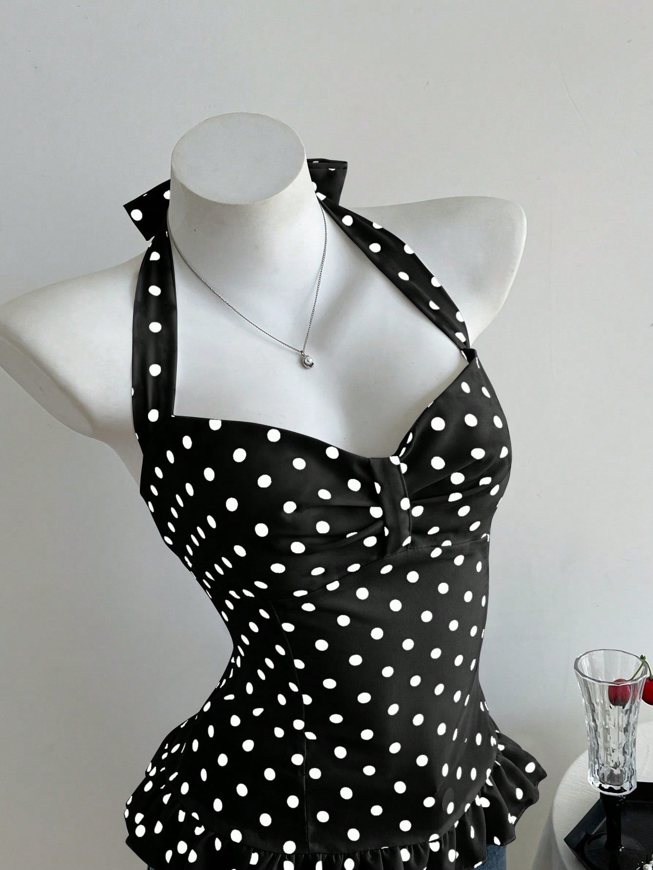Women's polka dot halter camisole with bow bust detail, ruched and shirred design, slim crop fit, and flared ruffle hem.