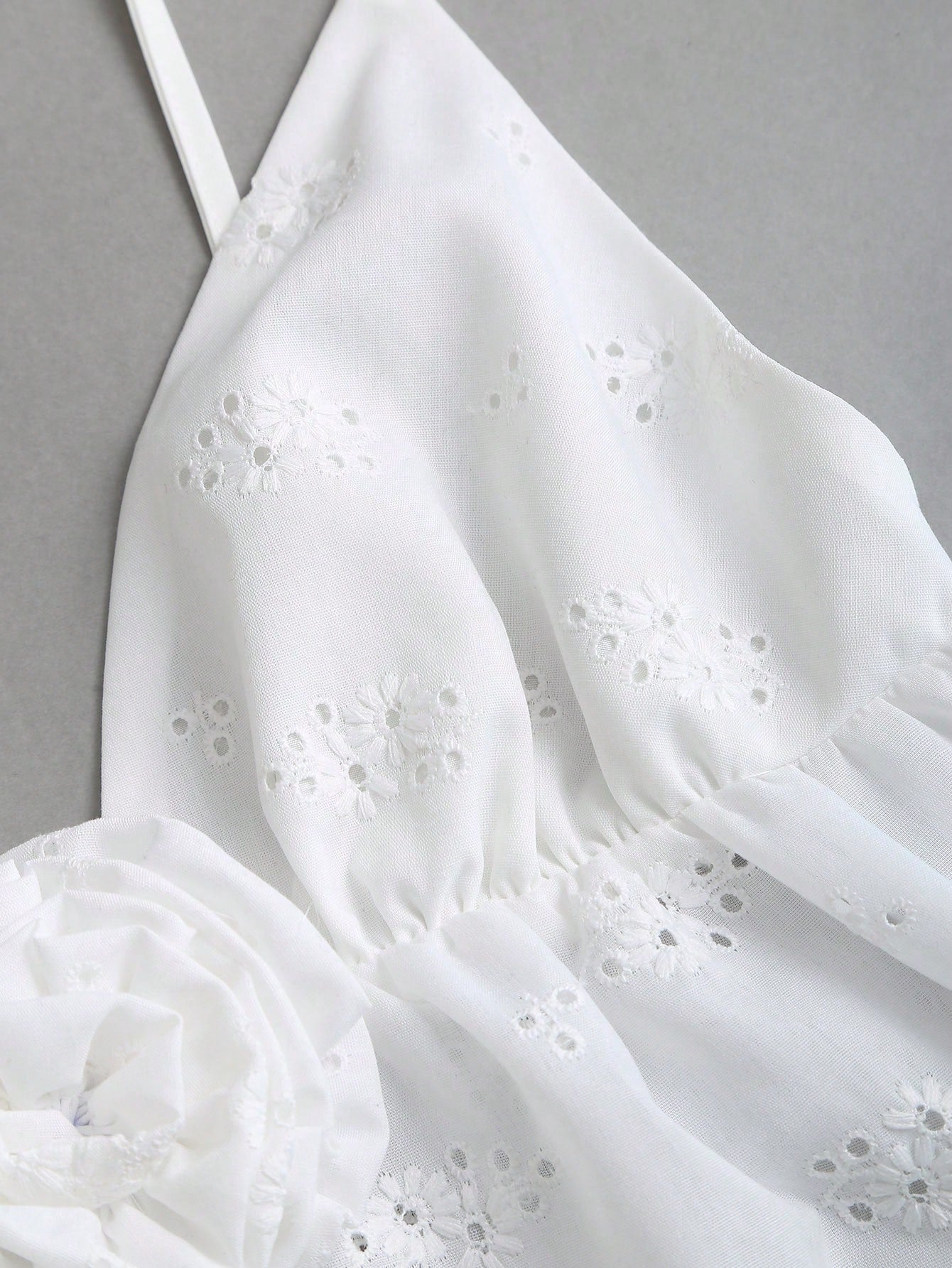 Women's white spaghetti strap cami top with eyelet embroidery, knot detail, ruffle hem, and flared hem shape