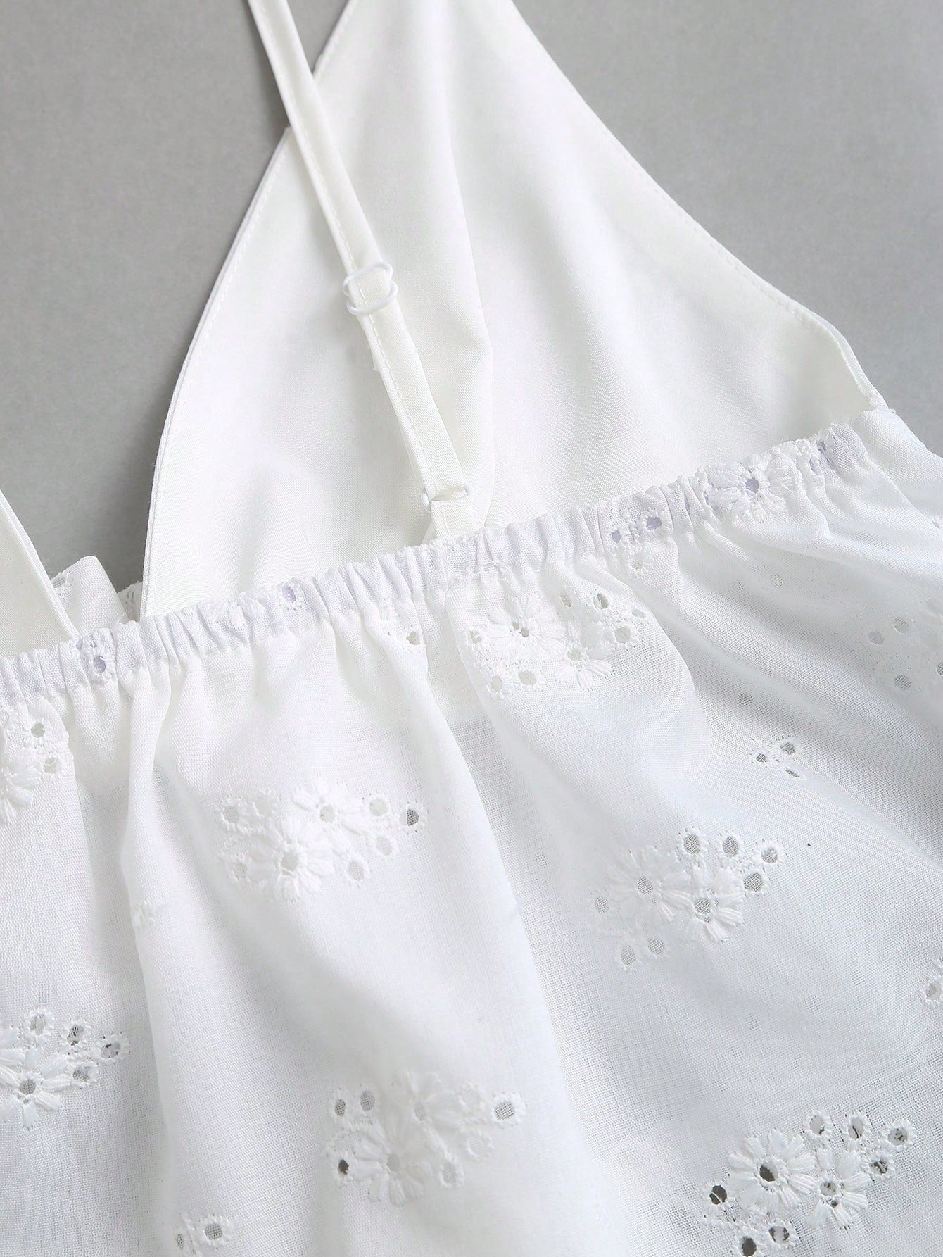 Women's white spaghetti strap cami top with eyelet embroidery, knot detail, ruffle hem, and flared hem shape