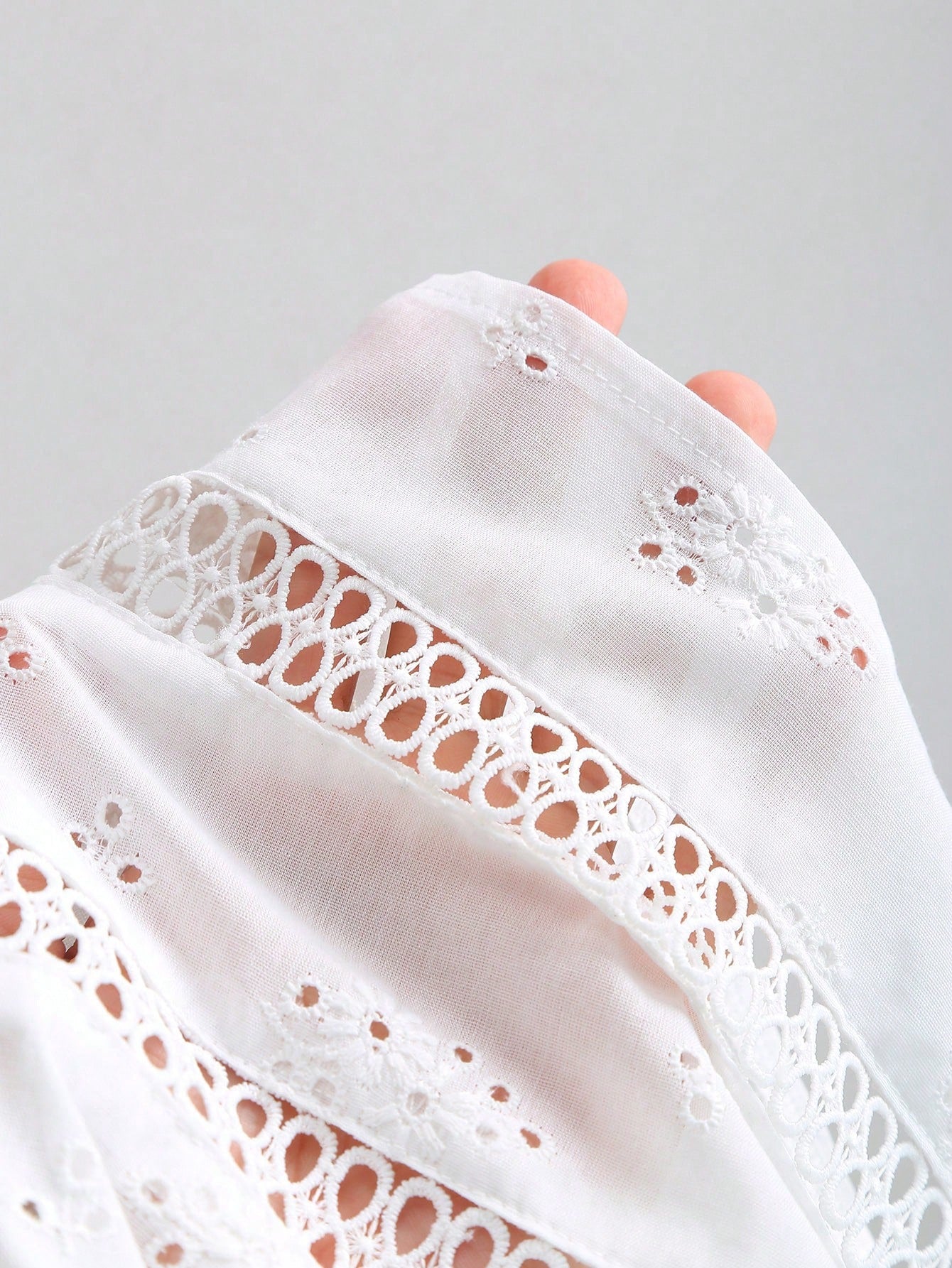 Women's white spaghetti strap cami top with eyelet embroidery, knot detail, ruffle hem, and flared hem shape