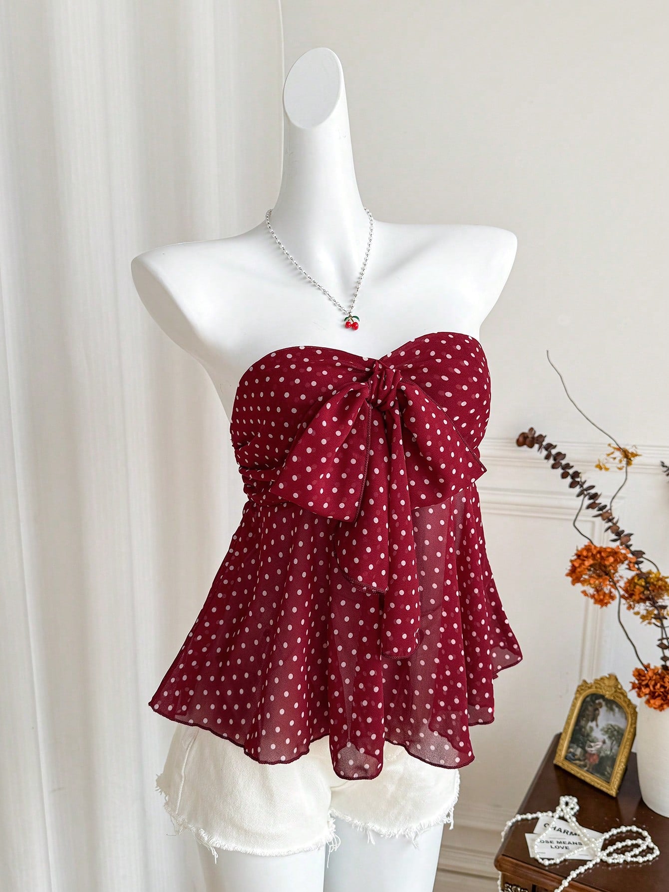 Women's polka dot strapless bandeau crop top with tie bow detail, asymmetrical shirring, and a flared hem.