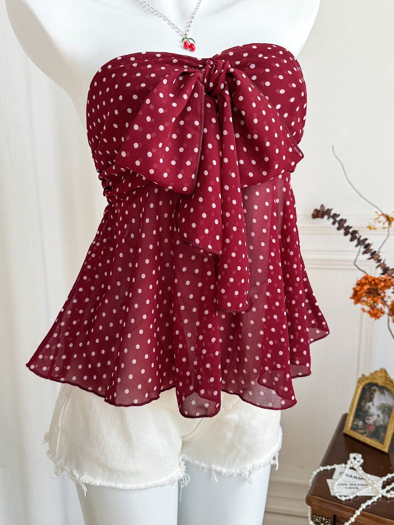 Women's polka dot strapless bandeau crop top with tie bow detail, asymmetrical shirring, and a flared hem.