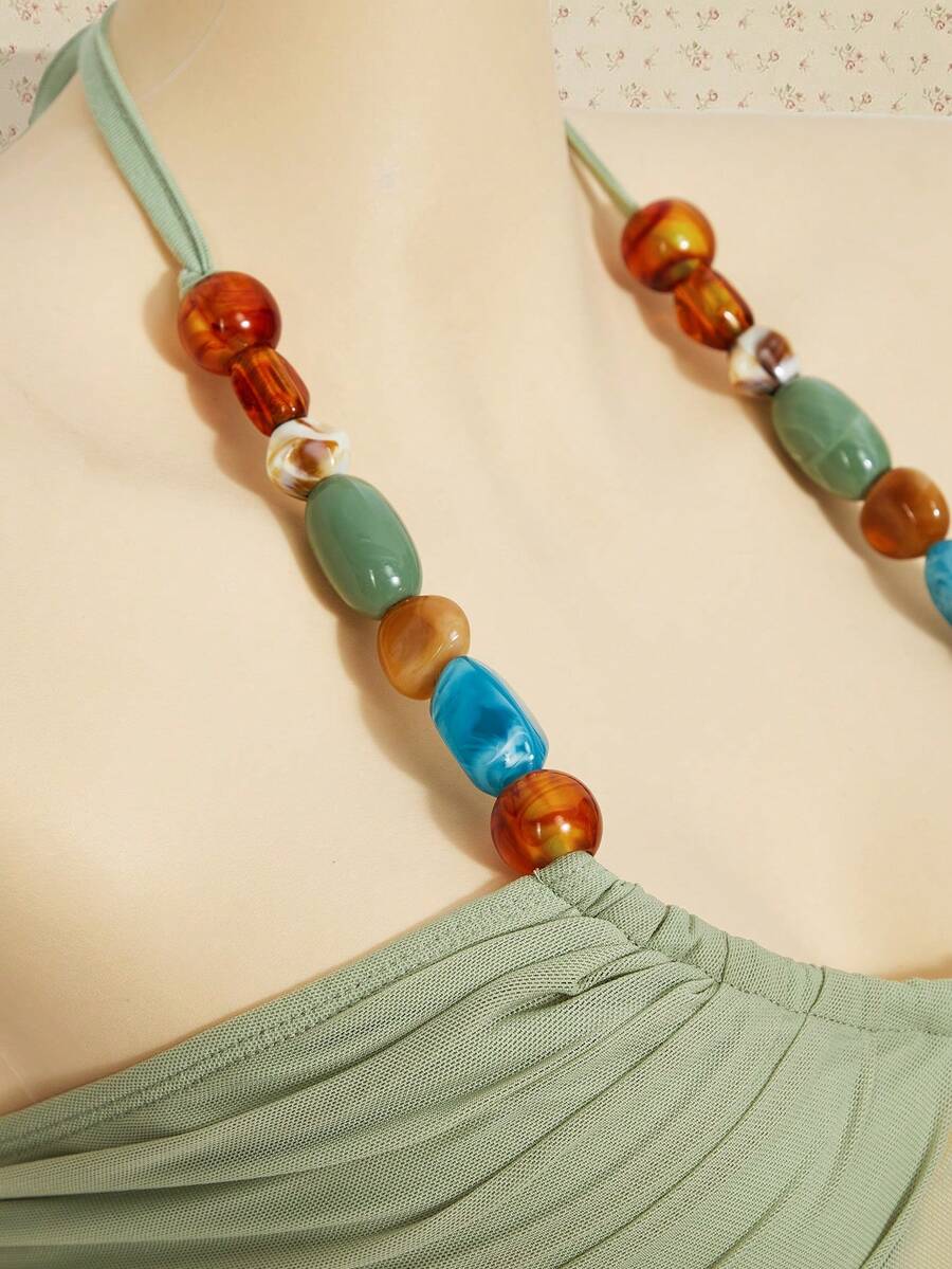 Women's boho halter mesh tank top with asymmetrical hem, semi-sheer finish, lined body, slim fit, and cold shoulder styling.