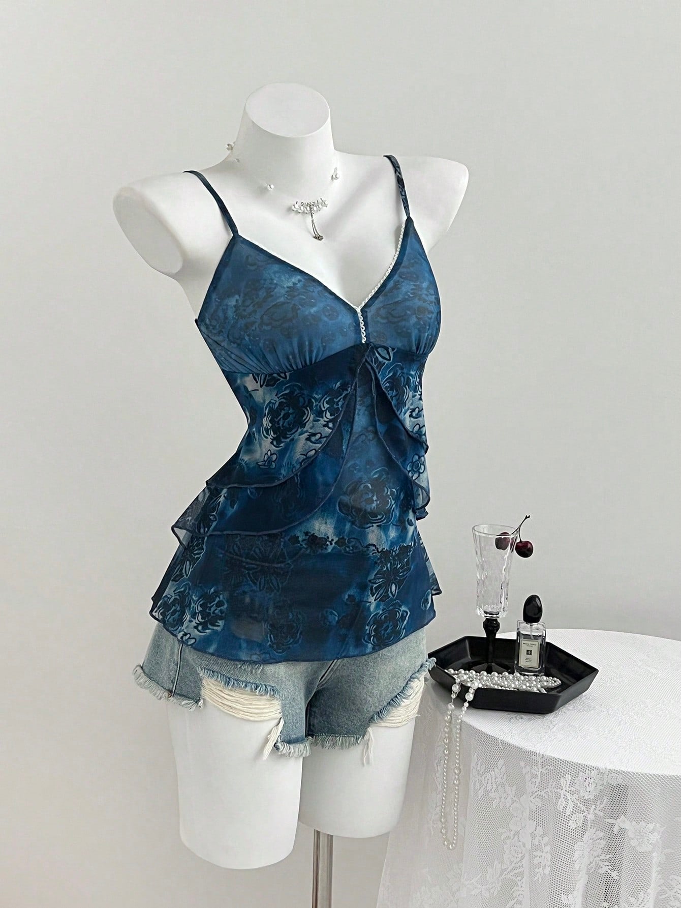 Women's boho spaghetti strap cami with multicolor all-over plant print, contrast lace detail, ruffle tiered hem, and slim fit silhouette.