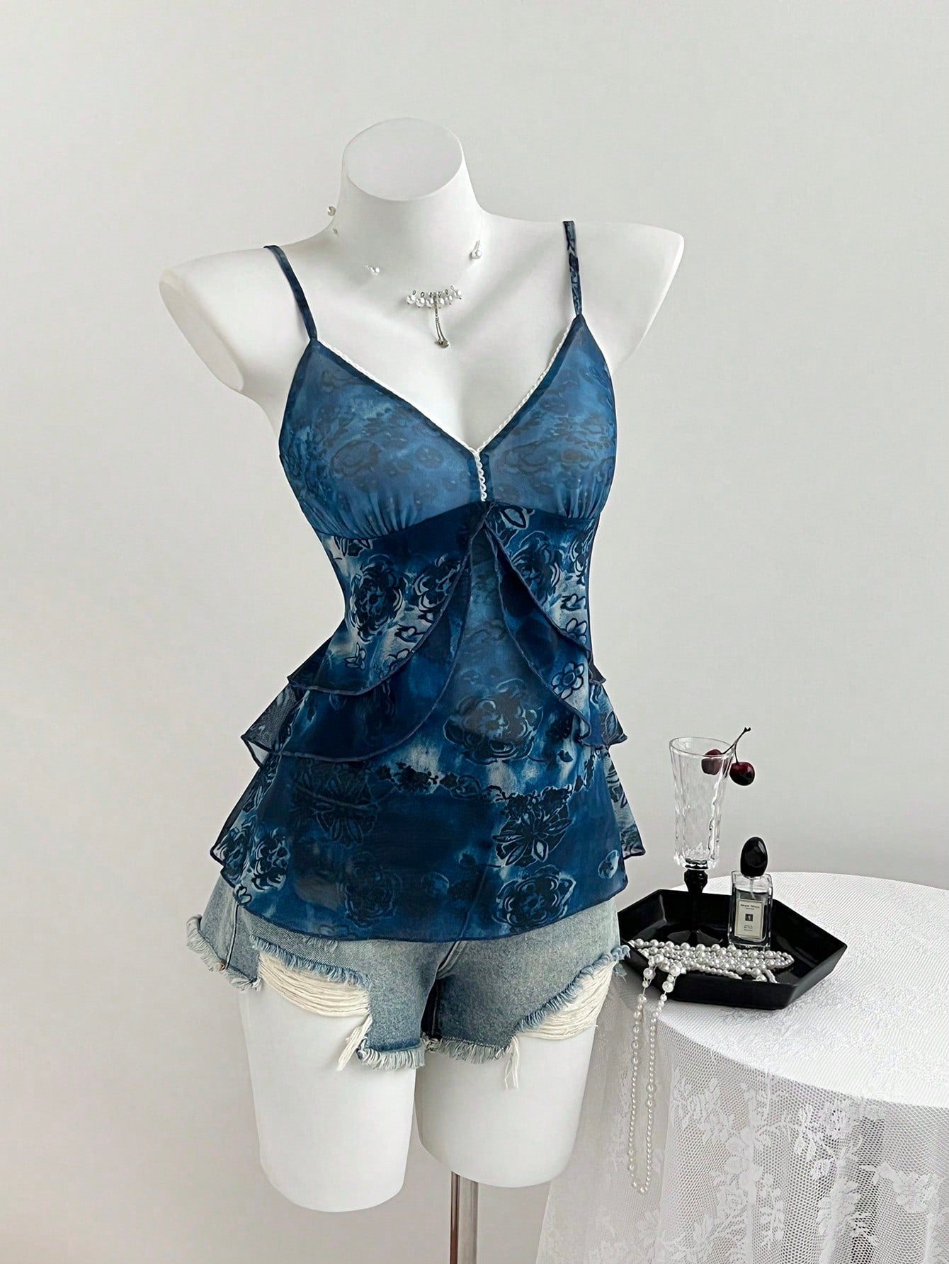 Women's boho spaghetti strap cami with multicolor all-over plant print, contrast lace detail, ruffle tiered hem, and slim fit silhouette.