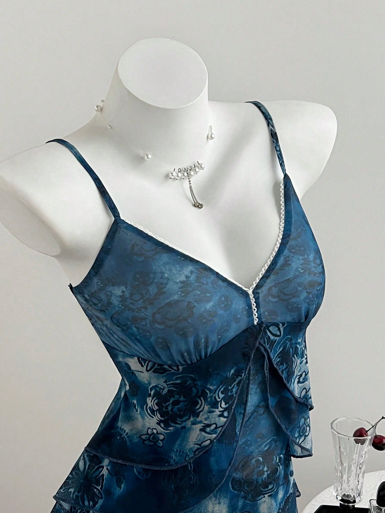 Women's boho spaghetti strap cami with multicolor all-over plant print, contrast lace detail, ruffle tiered hem, and slim fit silhouette.
