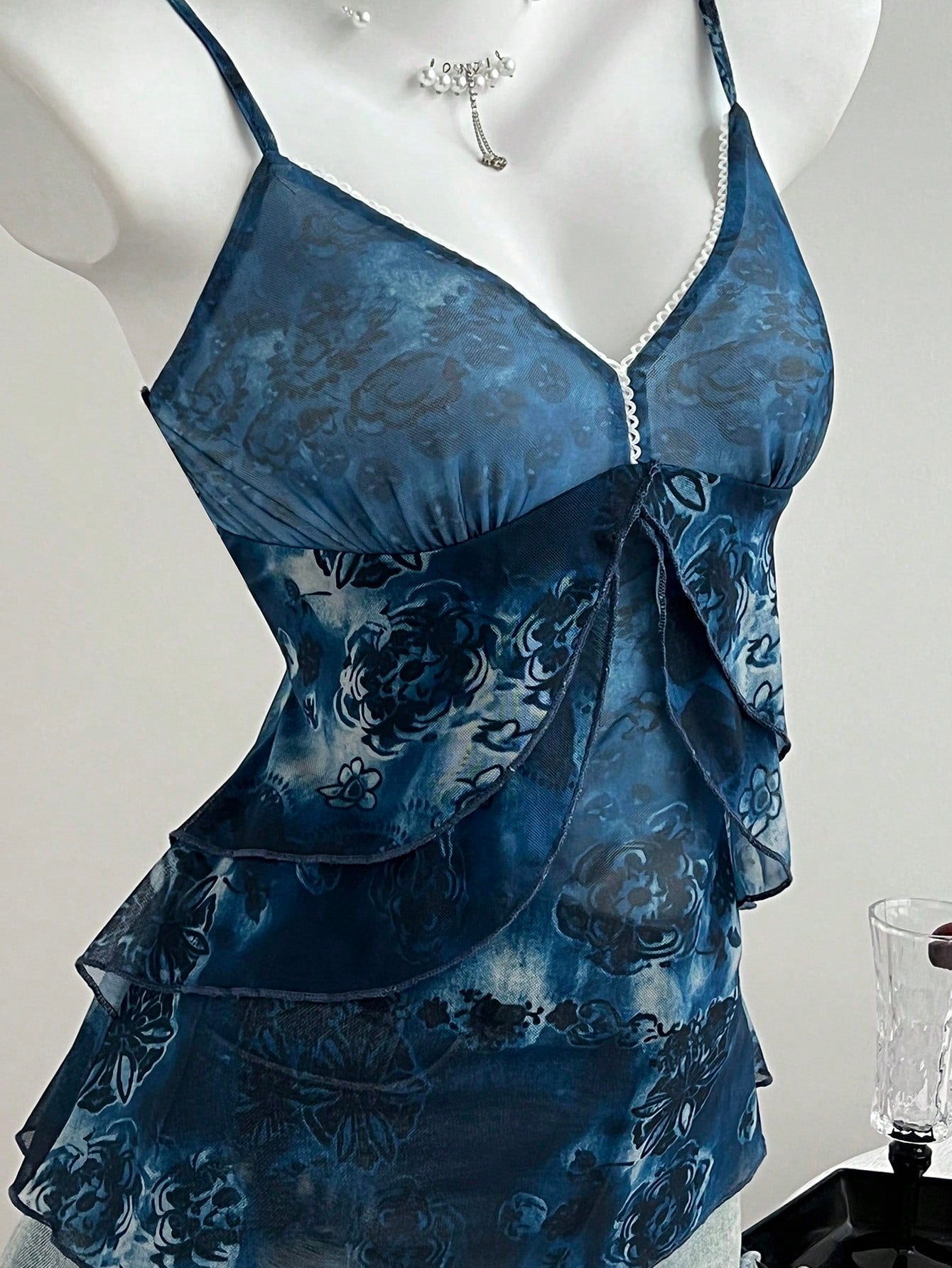 Women's boho spaghetti strap cami with multicolor all-over plant print, contrast lace detail, ruffle tiered hem, and slim fit silhouette.