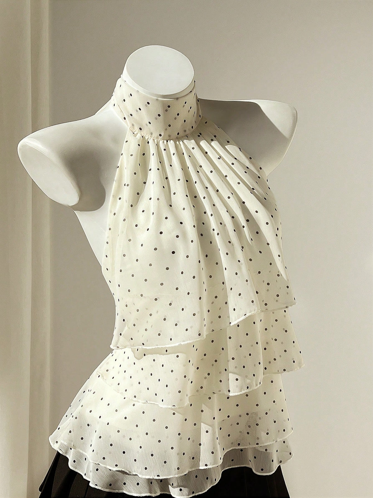 Women's white sleeveless halter neck top featuring pleated fabric, backless tie strap design, and a flared layered ruffle hem.