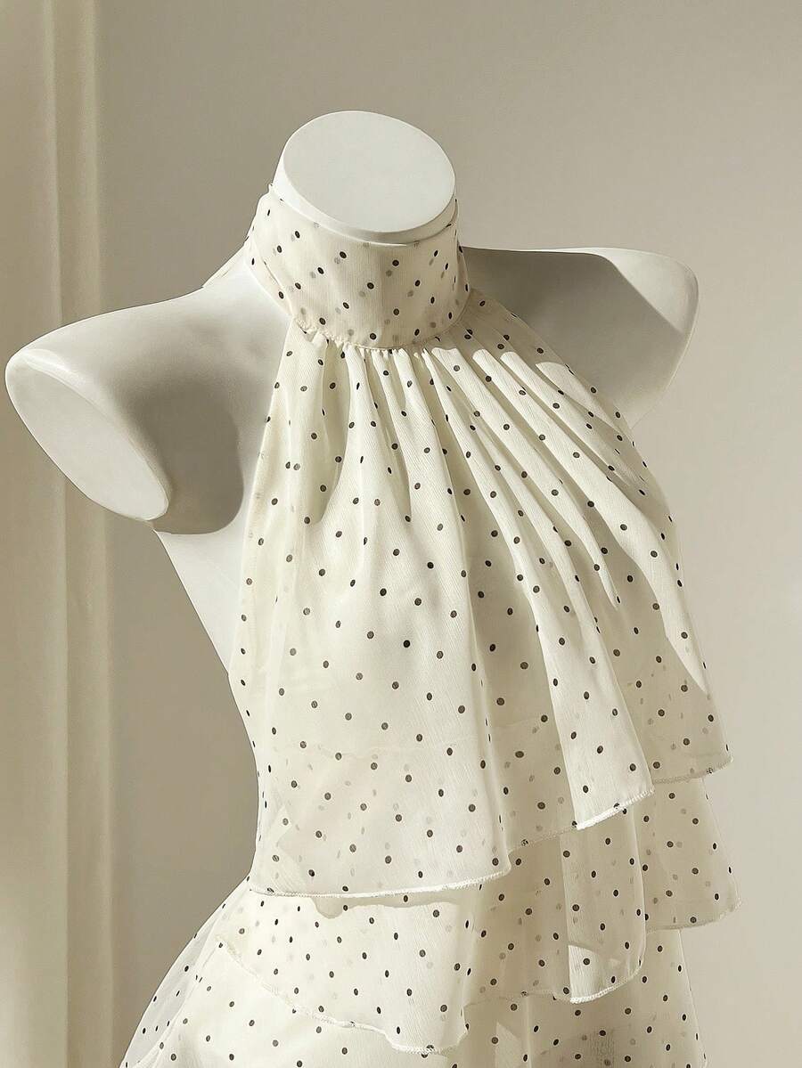 Women's white sleeveless halter neck top featuring pleated fabric, backless tie strap design, and a flared layered ruffle hem.
