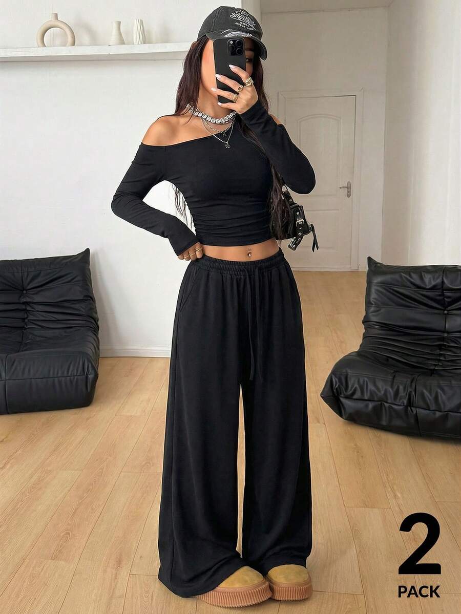Women's two-piece knit lounge set featuring a black long sleeve asymmetrical crop top and matching high-waisted wide leg sweatpants.