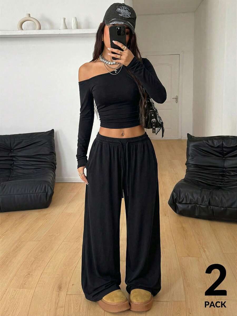 Women's two-piece knit lounge set featuring a black long sleeve asymmetrical crop top and matching high-waisted wide leg sweatpants.