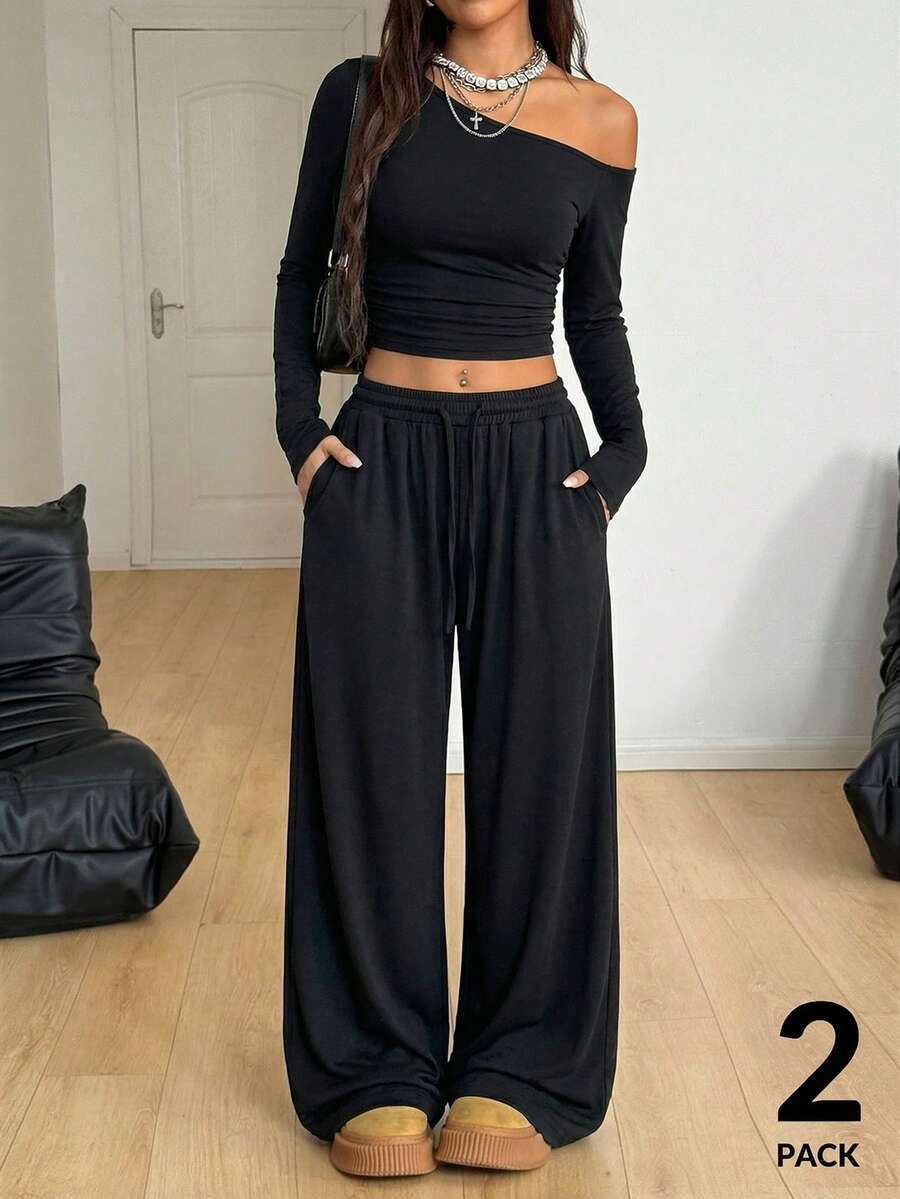 Women's two-piece knit lounge set featuring a black long sleeve asymmetrical crop top and matching high-waisted wide leg sweatpants.