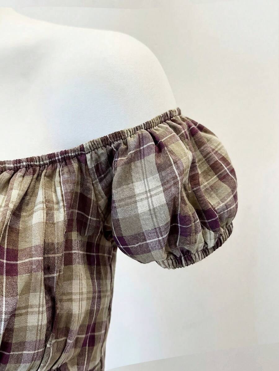 Women's army green plaid off-the-shoulder shirt with short puff sleeves, front button closure, flared hem, and lace-up grommet eyelet details.
