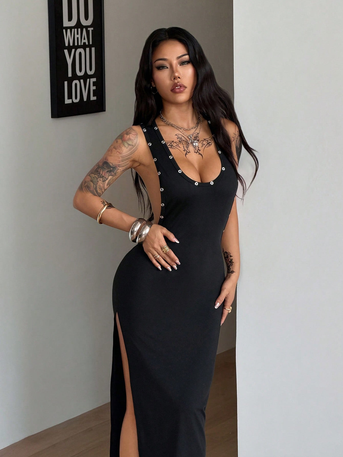 Front and side view of a women's black sleeveless bodycon maxi dress featuring a round neckline, open back, and high leg slit with metallic grommet eyelet details.