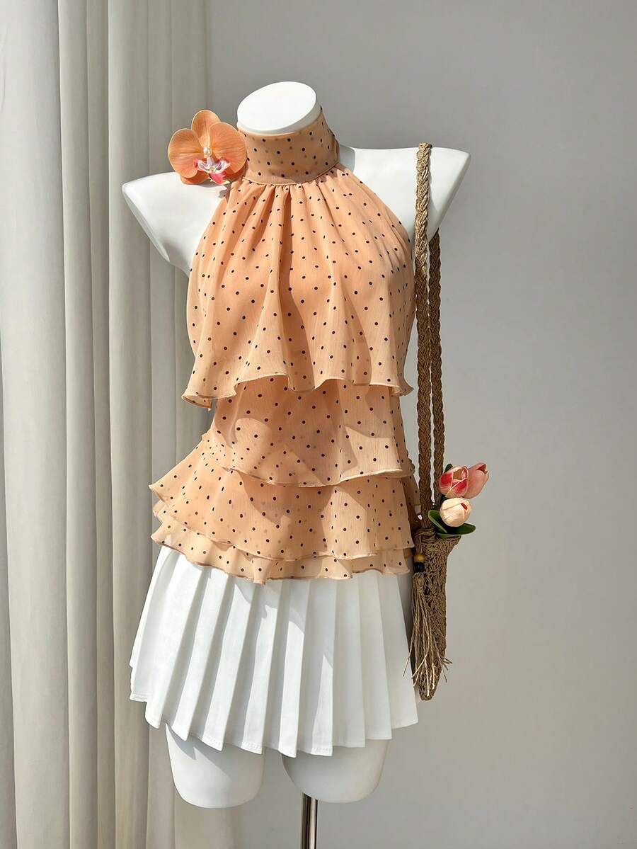 Women's white sleeveless halter neck top featuring pleated fabric, backless tie strap design, and a flared layered ruffle hem.