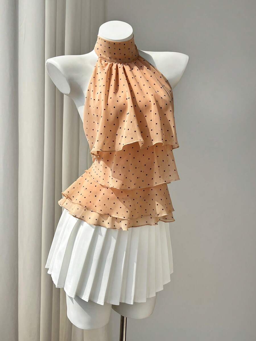 Women's white sleeveless halter neck top featuring pleated fabric, backless tie strap design, and a flared layered ruffle hem.