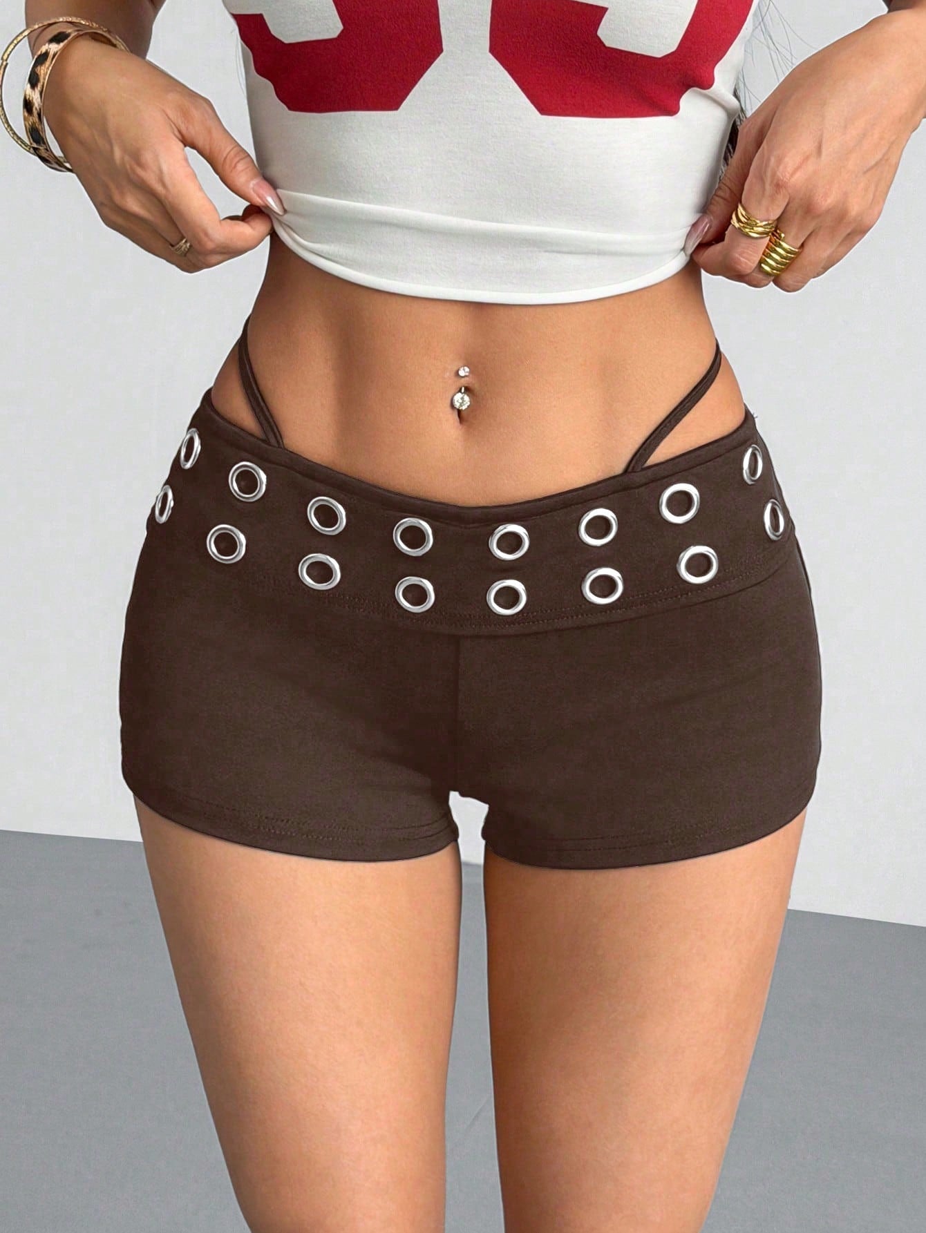Women's casual track shorts with elastic waist, low-rise mini length, colorblock graphic pattern, and cut-out studded grommet eyelet details.