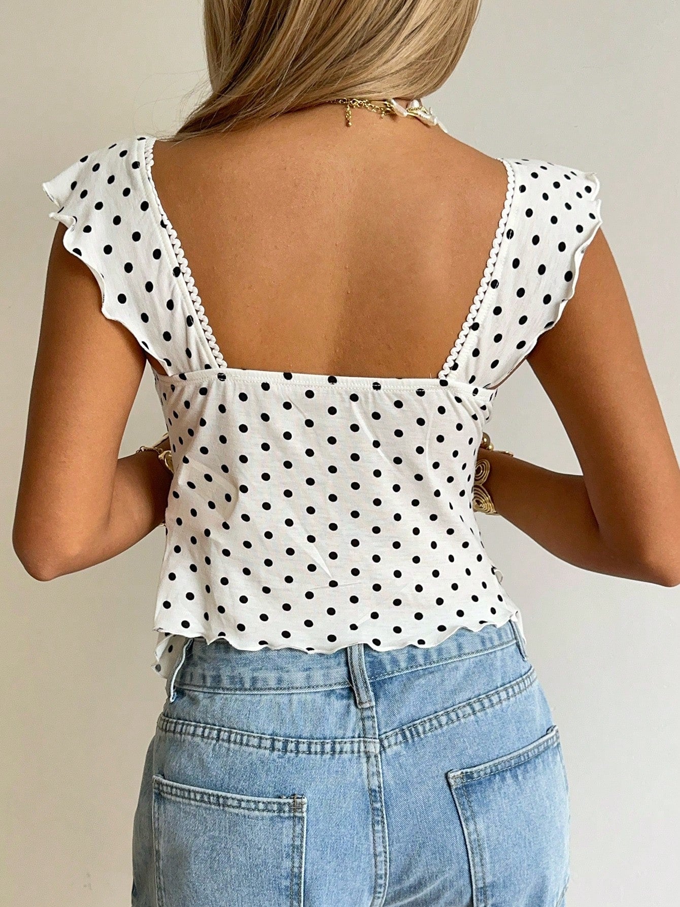 Women's black and white polka dot tank top with sweetheart neckline, twist detail, slim fit, and flared hem